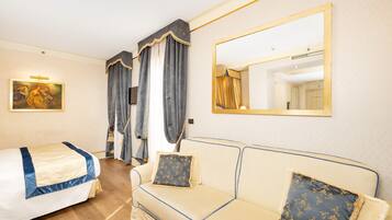 A hotel room with a bed, a sofa, a large mirror, and a painting on the wall.