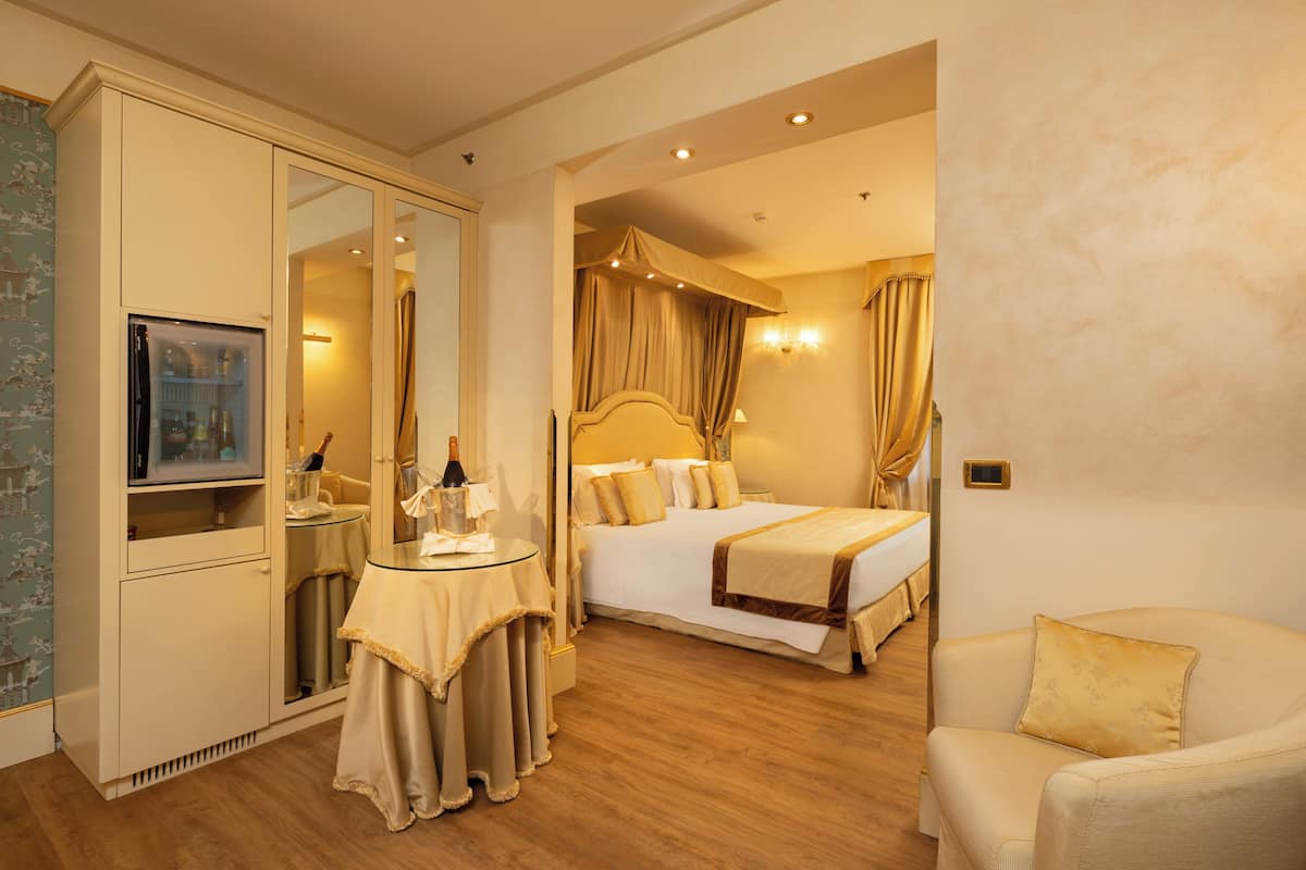 A hotel room with a bed, a sitting area, a table with a bottle, and a mirror.