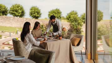 Un comedor con una mesa lista para tres personas, un camarero atendiendo y una vista de un viñedo al fondo.
