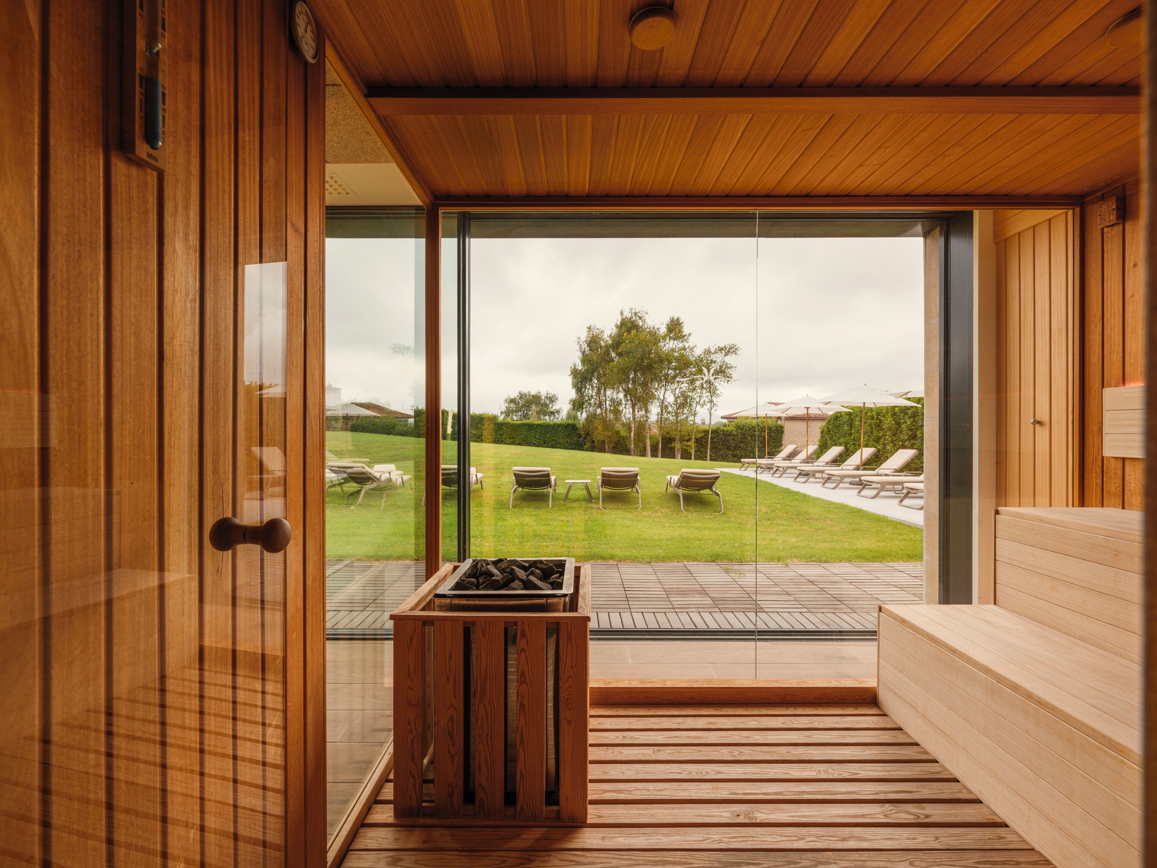Interior moderno de madera con un gran ventanal que da a un espacio exterior con sillones de descanso y un banco de madera.