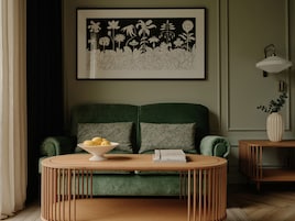 A green sofa with a bowl of lemons and a book on a round wooden table.