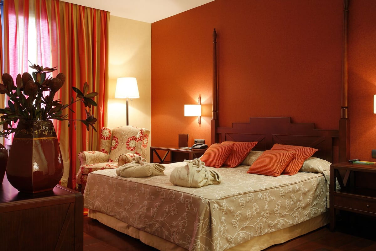 A hotel room with a bed, bedside tables, a lamp, a chair, and a vase with flowers.