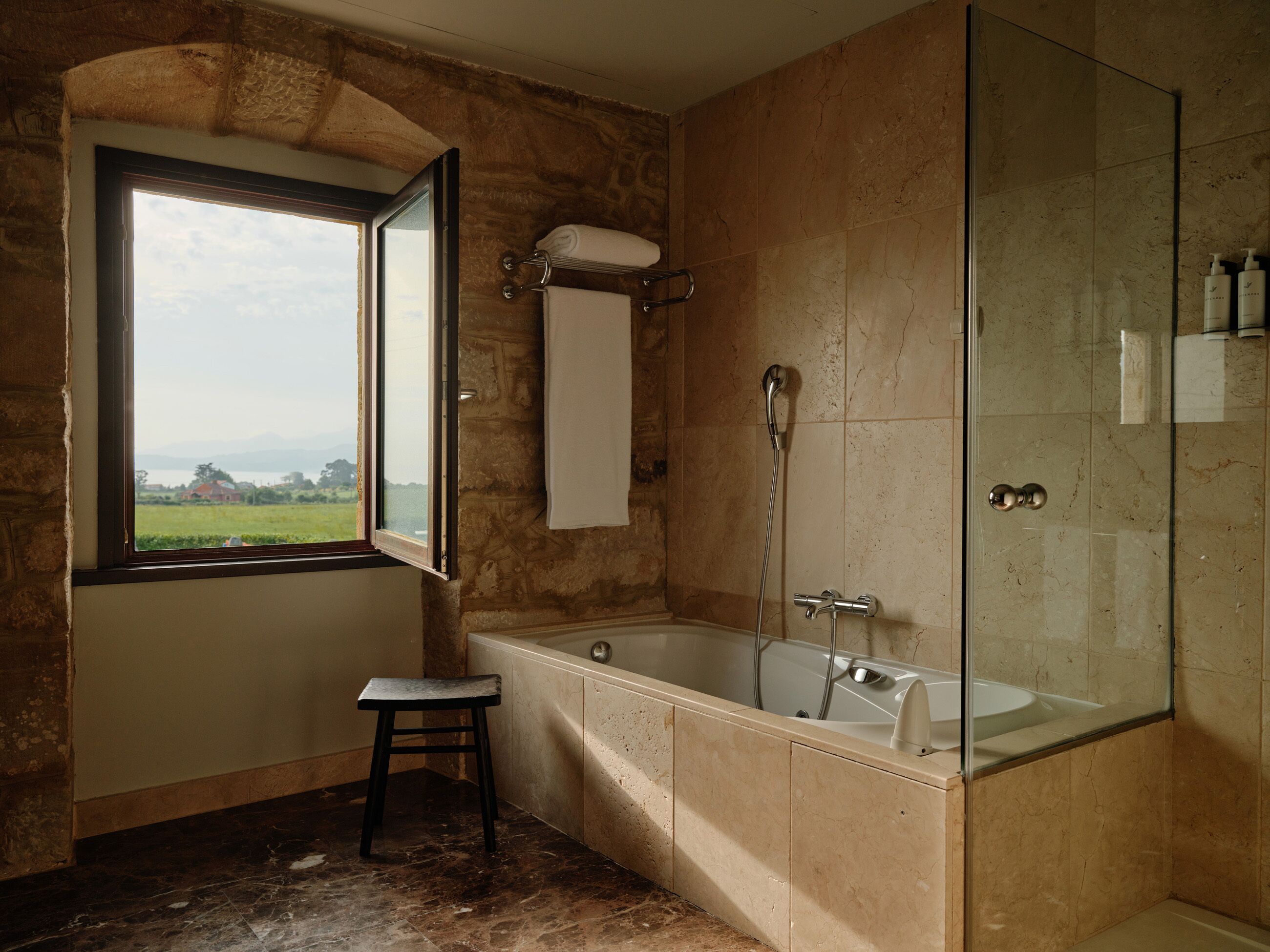 Un baño con bañera, ducha, ventana con vistas y un perchero para toallas.