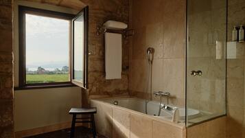Un baño con bañera, ducha, ventana con vistas y un perchero para toallas.