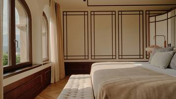A bedroom with a large bed, a window with curtains, a wooden floor, and a view of the outdoors.