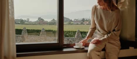 Une personne est assise près d’une fenêtre donnant sur un paysage composé de constructions en pierre et de verdure.