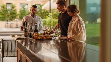 Una zona de bar con una barra larga, copas de vino, botellas y vistas al exterior.