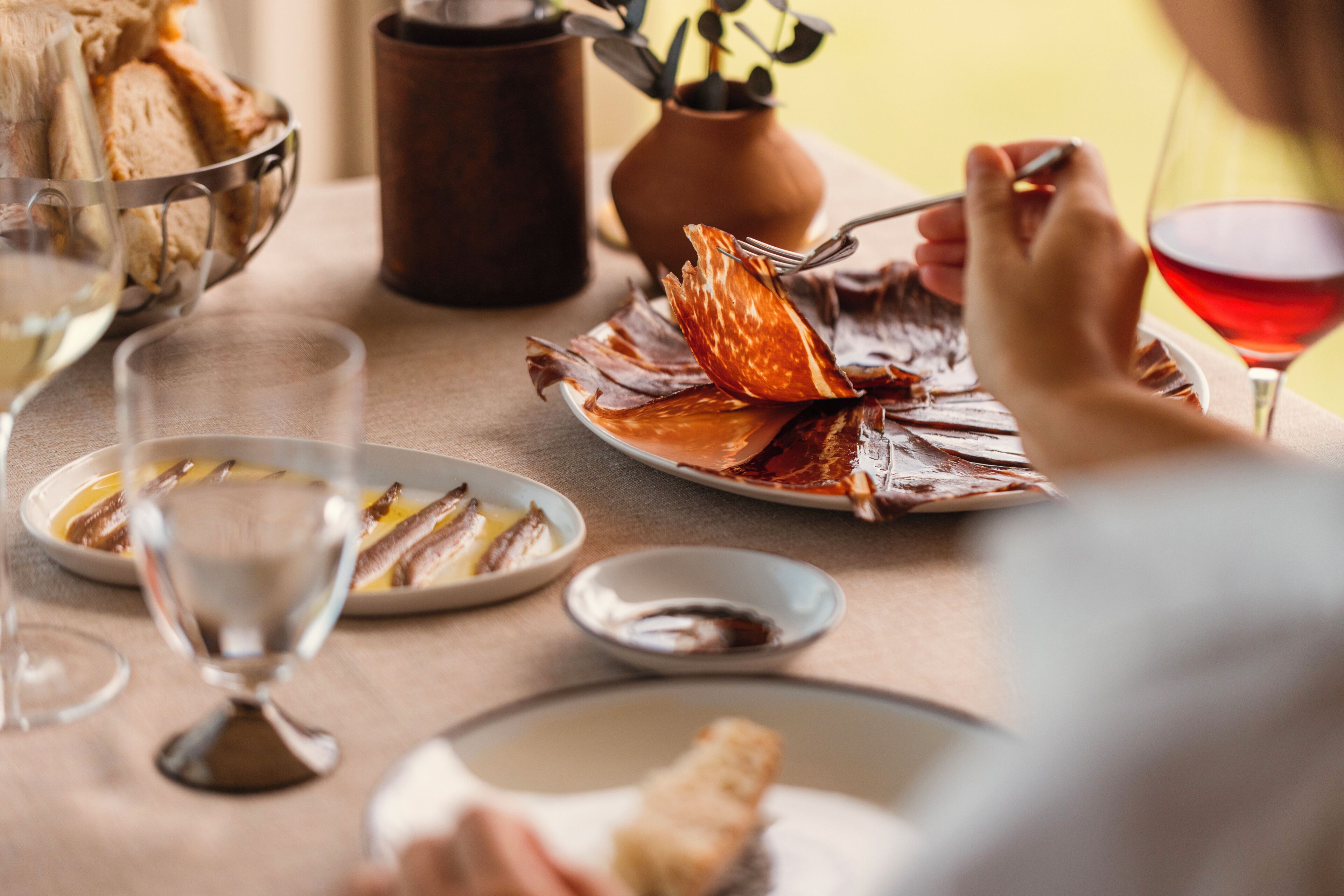 Une table à manger avec des assiettes remplies de nourriture, des verres de vin et un vase.