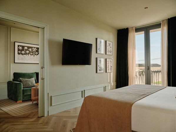 Habitación de hotel con cama, televisor, sillón verde y balcón con vistas.