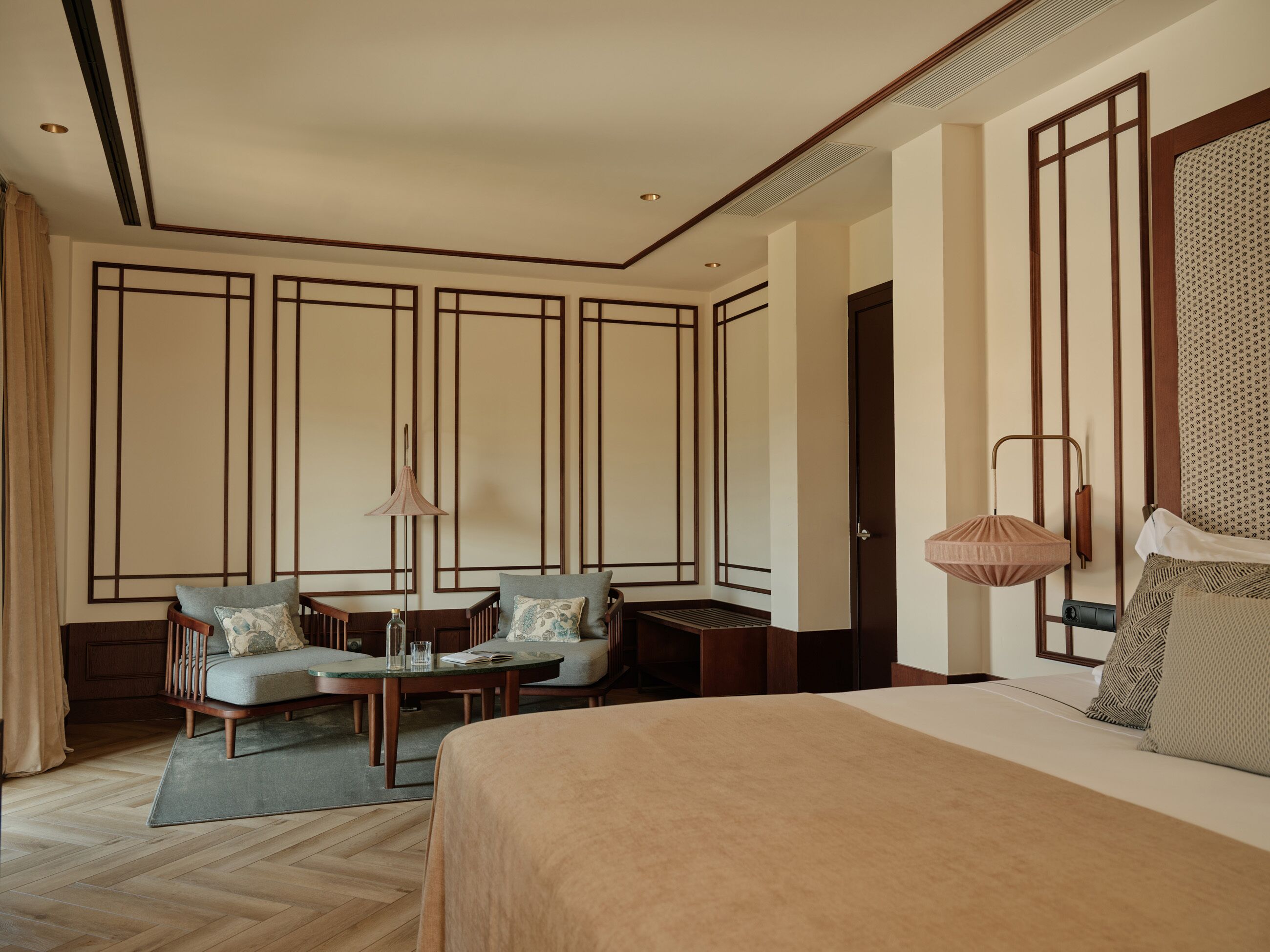 Een hotelkamer met een bed, twee fauteuils, een tafeltje en een lamp.