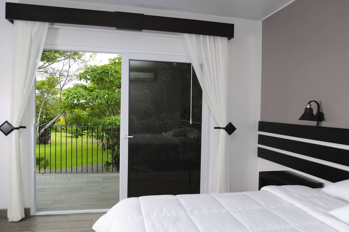 A bedroom with a large bed, a sliding glass door to a balcony, and a nightstand with a lamp.