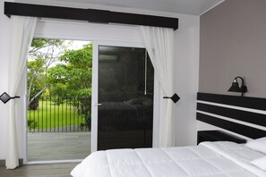 A bedroom with a large bed, a sliding glass door to a balcony, and a nightstand with a lamp. - Hotel Robledal (San Antonio)