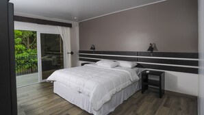 A bedroom with a large bed, a nightstand, a ceiling light, and a sliding glass door leading to a balcony. - Hotel Robledal (San Antonio)