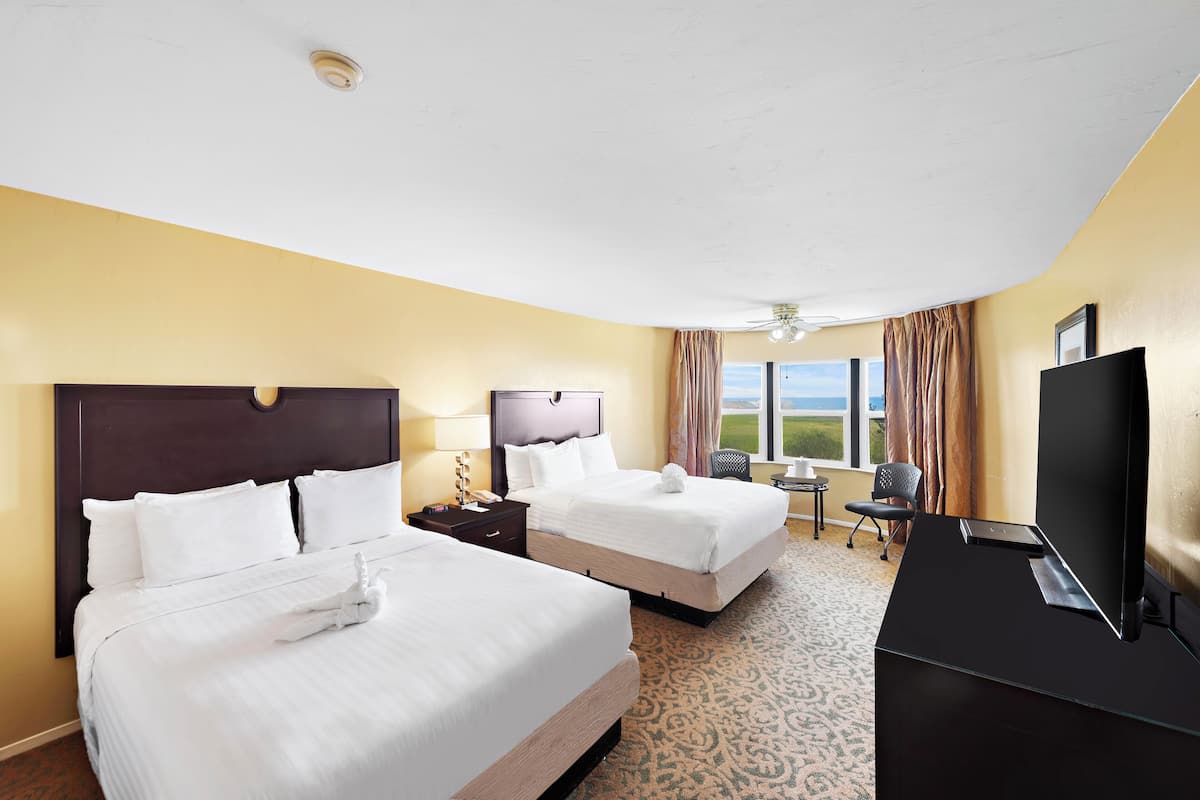 A hotel room with two beds, a desk, a TV, and a view of the outdoors.