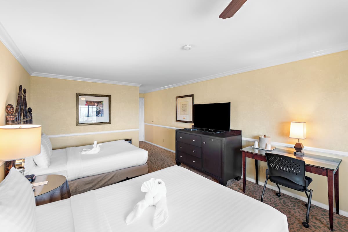 A hotel room with two beds, a desk, a chair, a television, and a lamp.