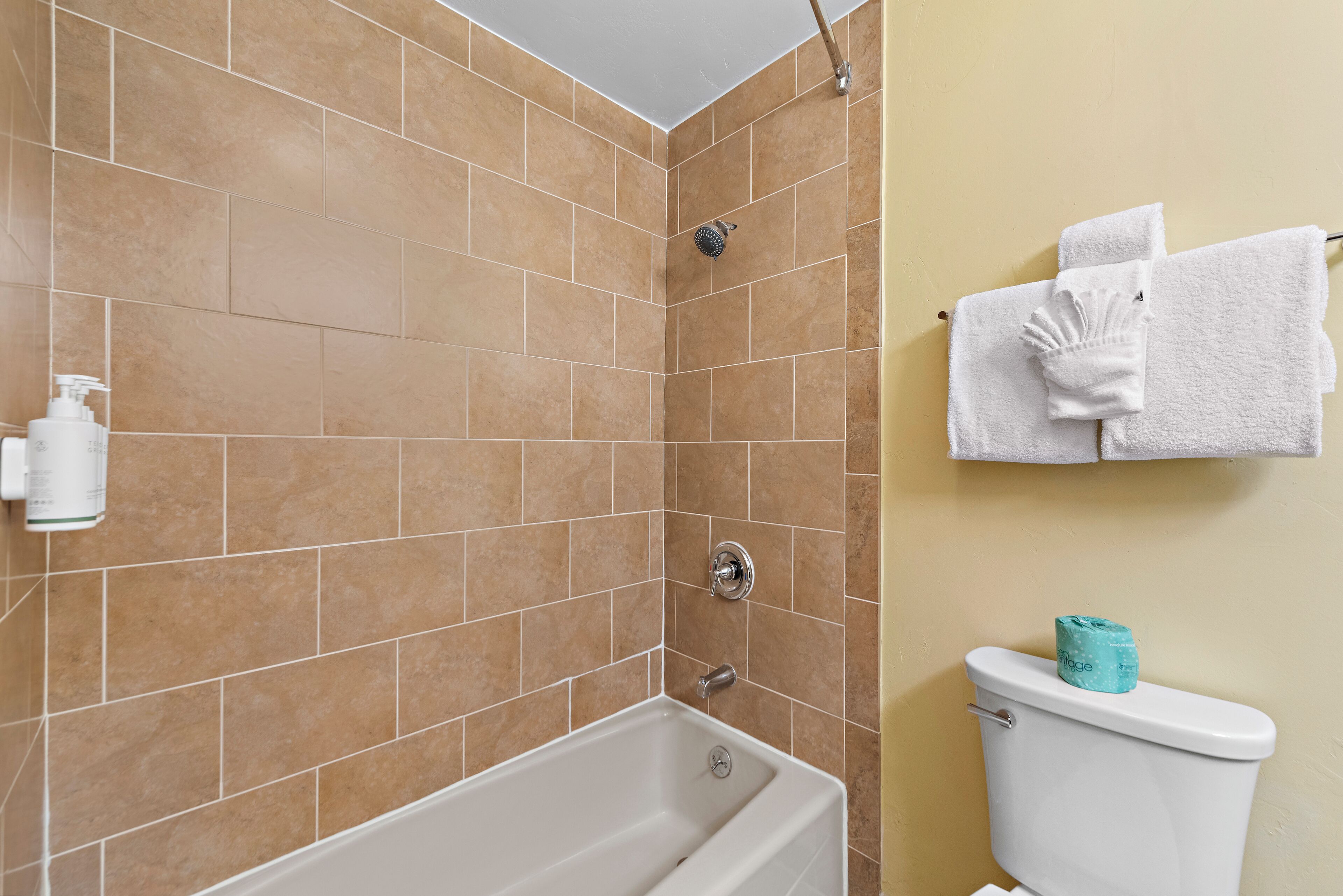 Un baño con baldosas color beige, una bañera blanca, un inodoro y un perchero con toallas.