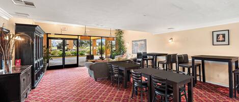 A hotel lobby with a red carpet, a reception desk, a sofa, and a dining area with tables and chairs.