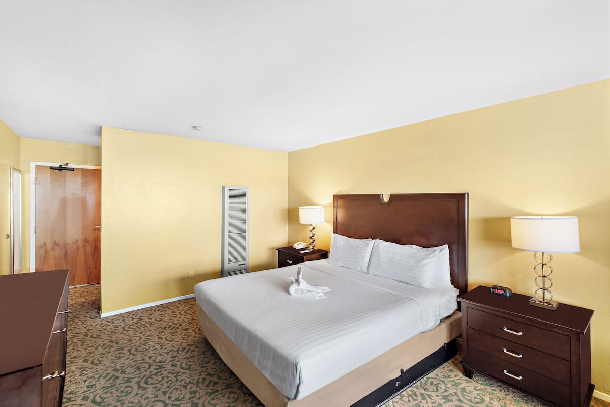 A hotel room with a large bed, two bedside tables with lamps, a wooden wardrobe, and a patterned carpet.