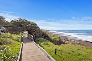 A wooden boardwalk leading to a beach with a large tree on the left. - The Morgan San Simeon - Cambria by Hearst Castle (San Simeon)