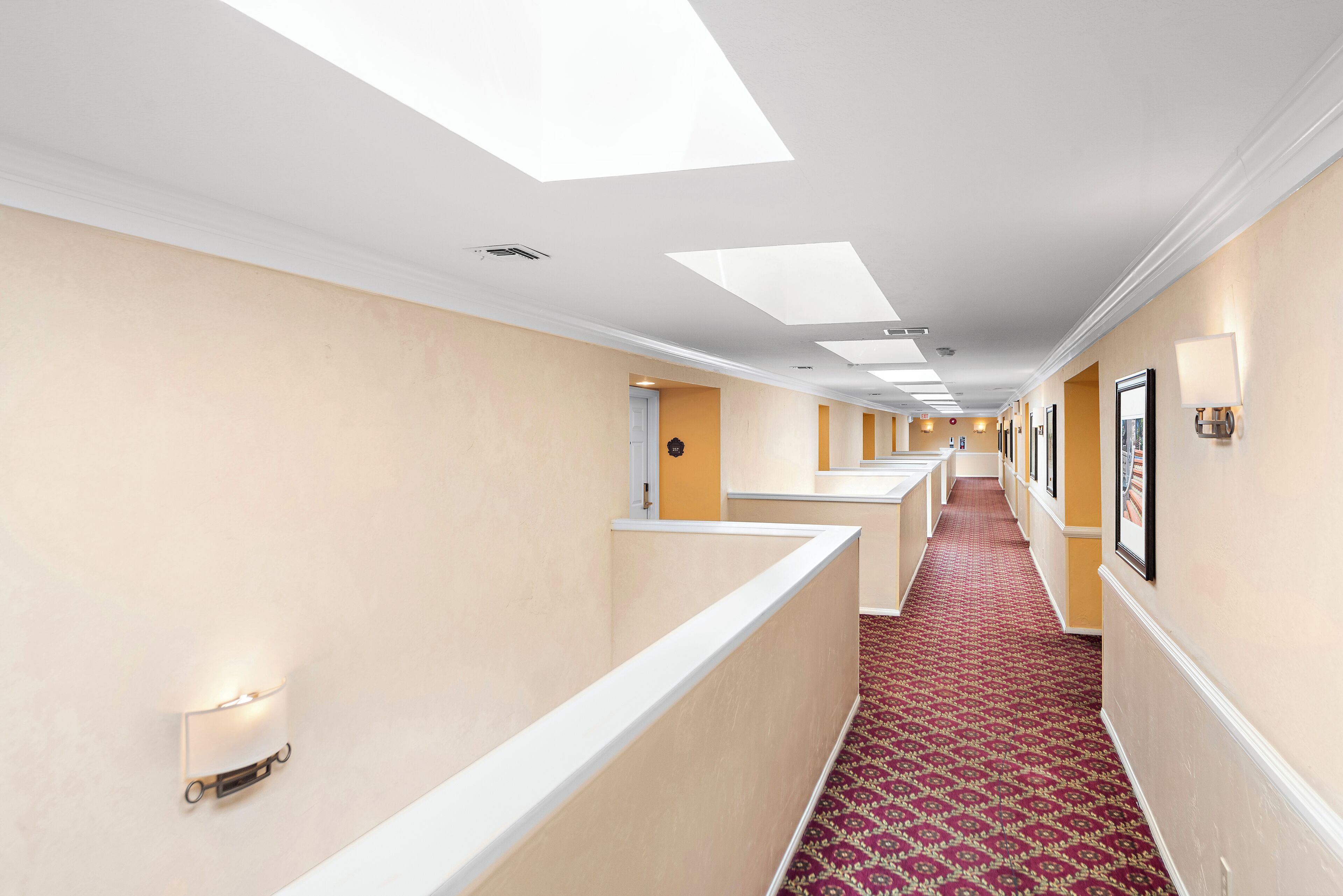 Un corridoio d'hotel con lucernari, illuminazione a incasso e tappeto a motivi.