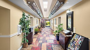 A hallway with patterned carpet, potted plants, a reception desk, and a large mirror.
