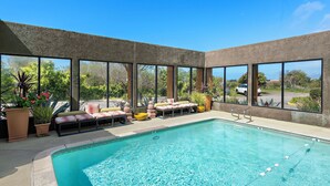 A swimming pool with lounge chairs and potted plants, surrounded by large windows.