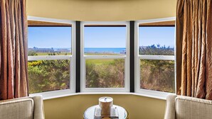 A room with a curved ceiling, three large windows offering a view of greenery and a distant landscape. A small table with a candle is in the center.