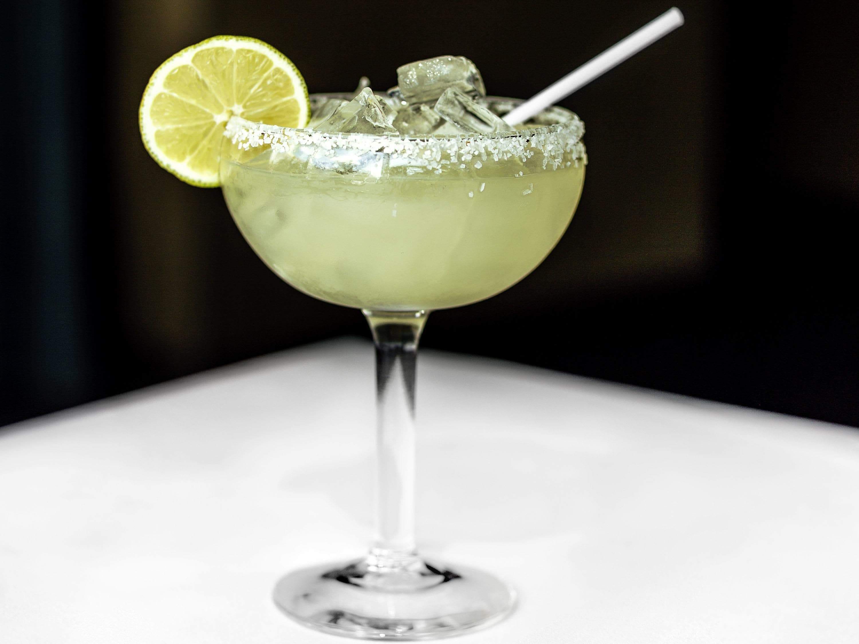 A margarita cocktail in a glass with a salted rim, a lime wedge, and ice cubes.