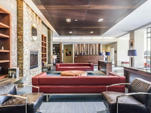 A lobby with a stone wall, a fireplace, red sofas, and a reception desk. - Novotel Montreal Aeroport (Montreal)