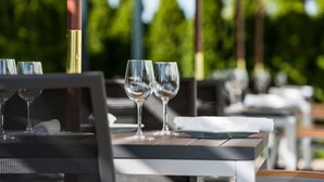 A dining table with two empty wine glasses and a folded napkin, set outdoors with a blurred green background. - Novotel Montreal Aeroport (Montreal)