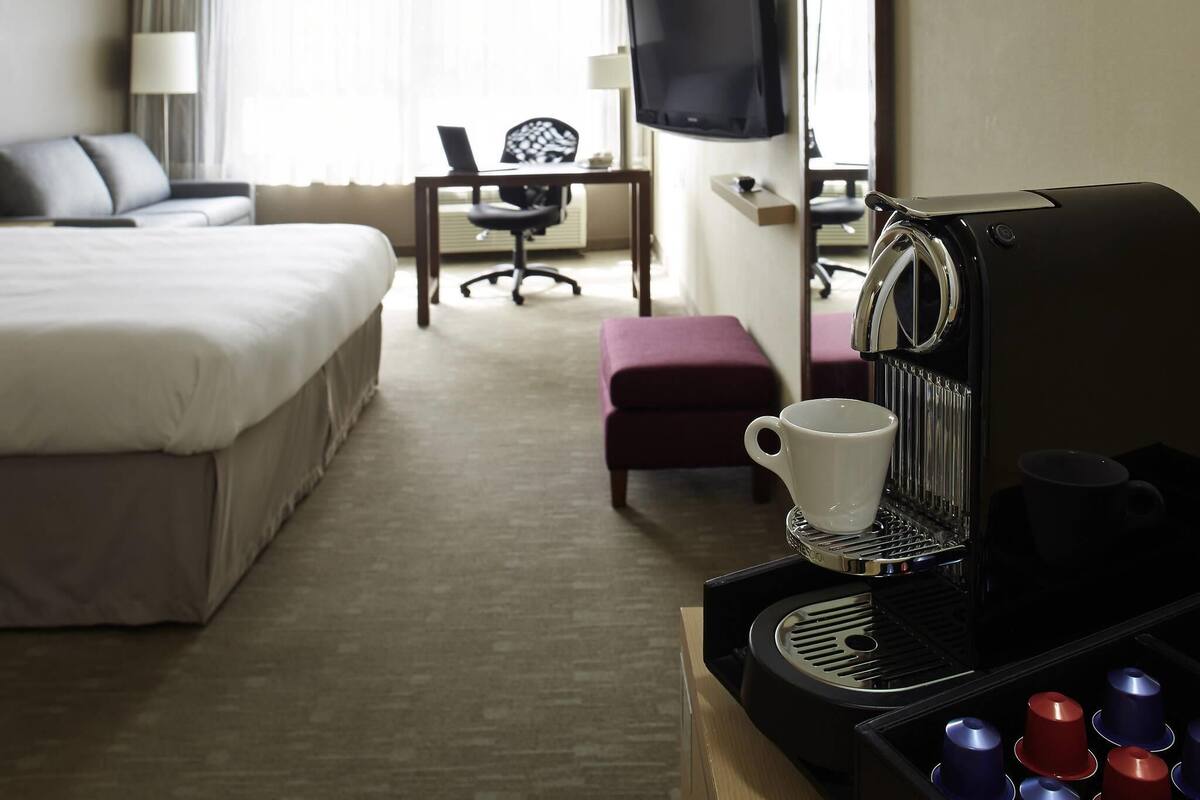 Habitación de hotel con cama, escritorio, silla, televisor y cafetera.