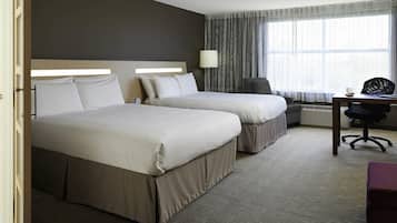 A hotel room with two beds, a desk with a chair, a lamp, and a large window with curtains.