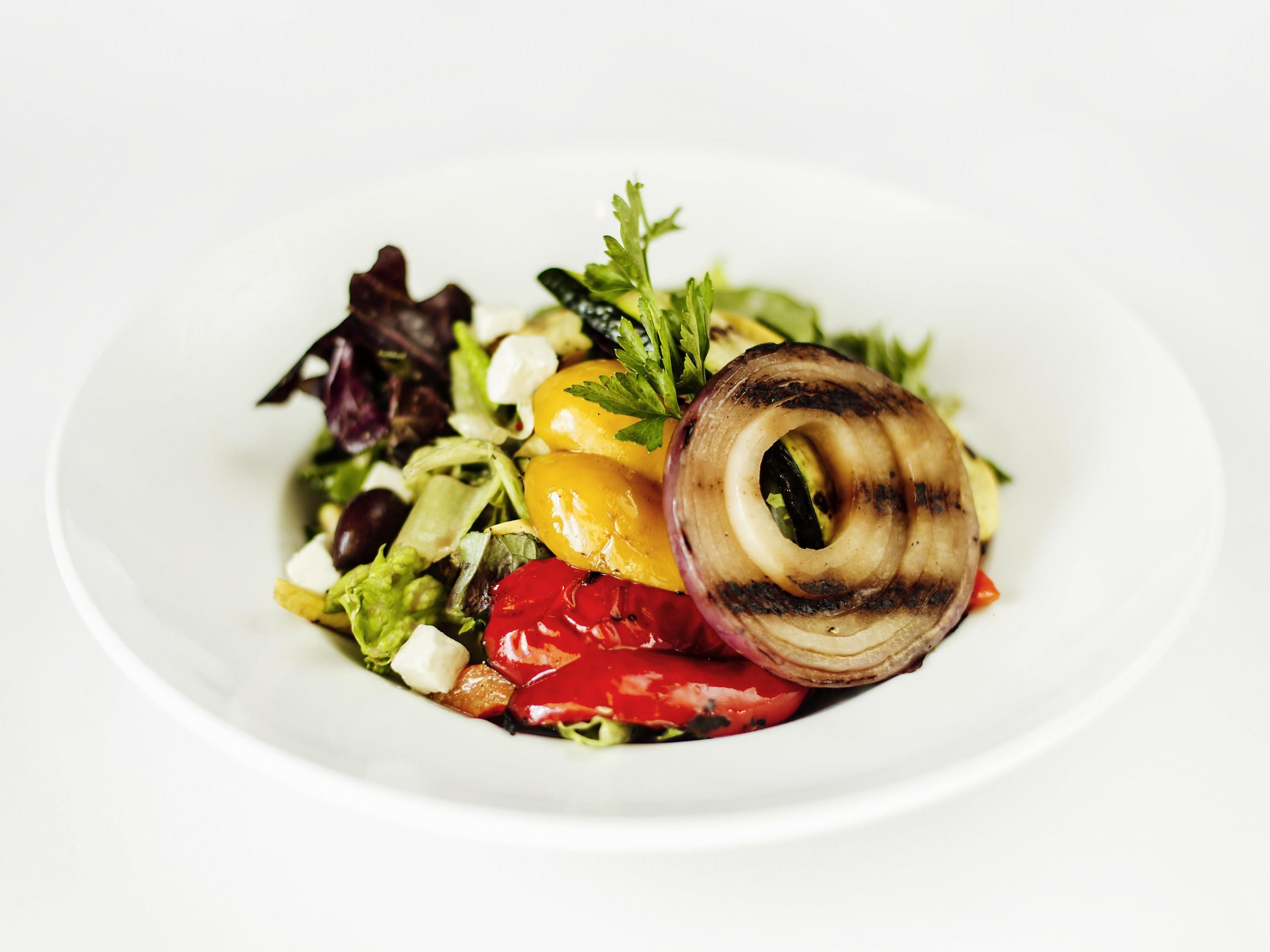 A white plate with a salad containing lettuce, tomatoes, and a grilled onion.
