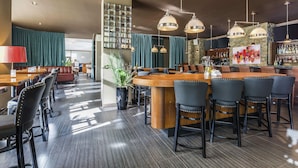 A bar area with a wooden counter, black bar stools, and pendant lighting. - Novotel Montreal Aeroport (Montreal)