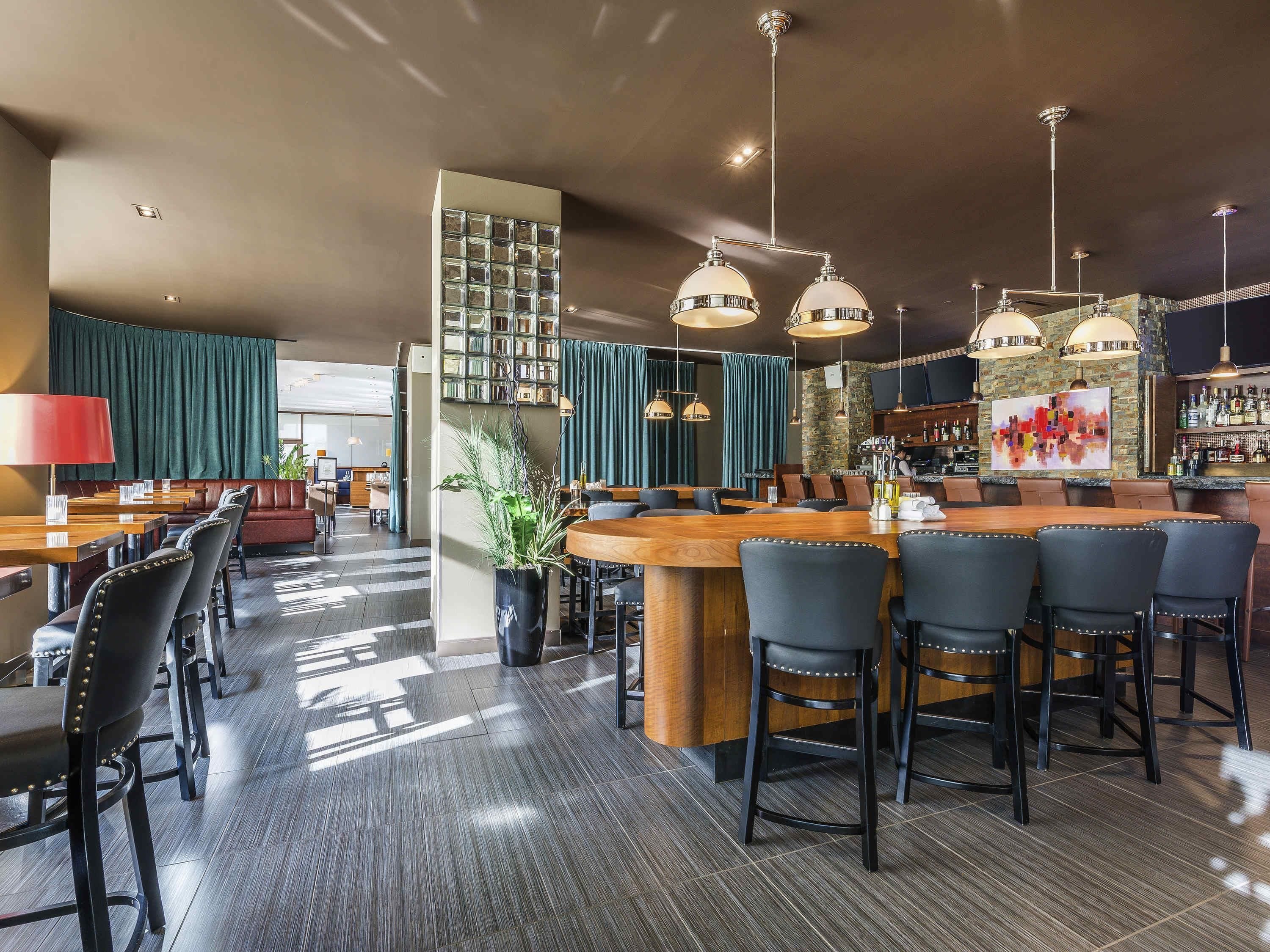 Una zona de bar con mostrador de madera, taburetes negros y lámparas colgantes.