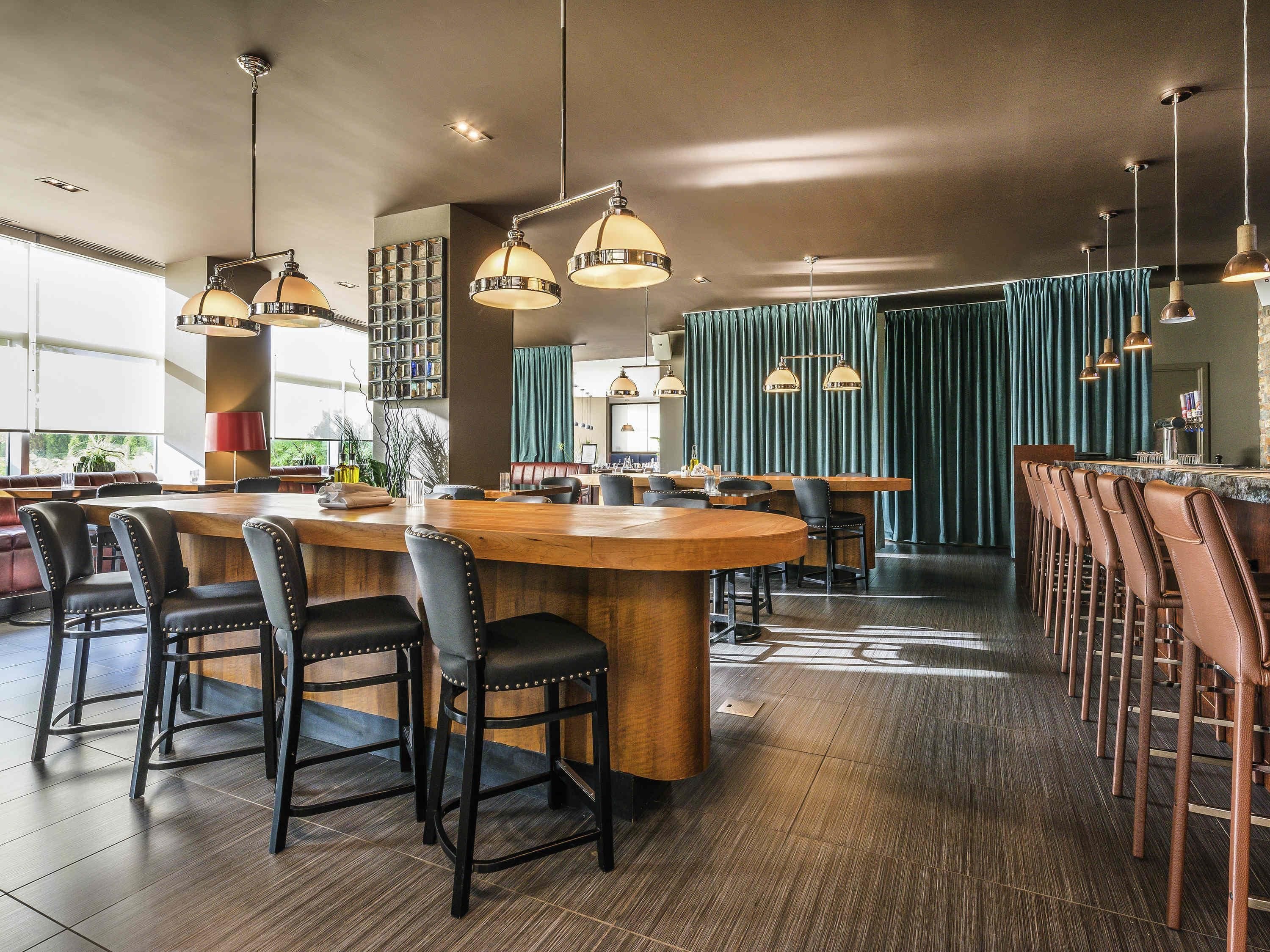 A modern bar area with wooden bar counters, leather bar stools, and pendant lighting.