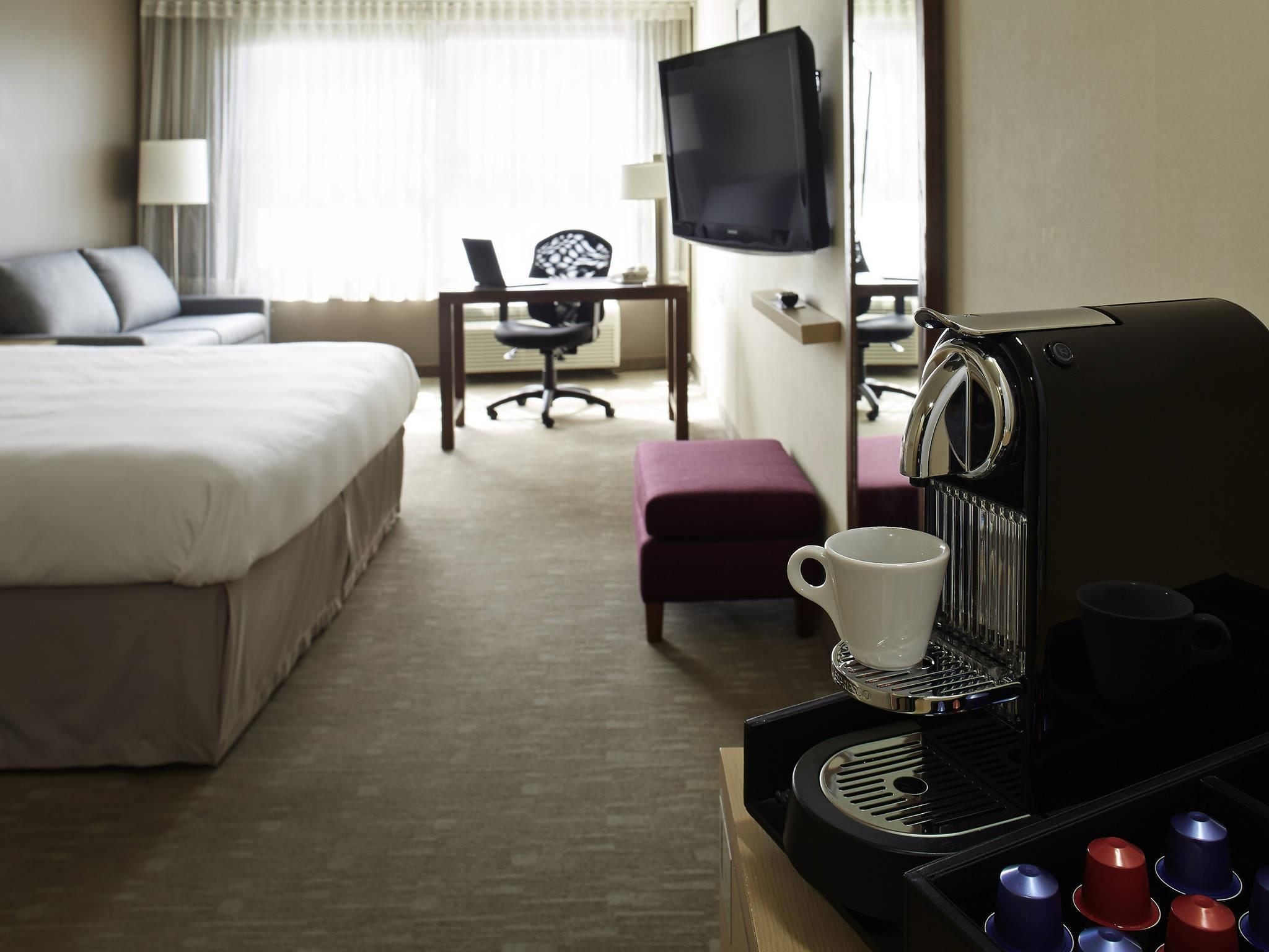 Habitación de hotel con cama, escritorio, silla, televisor y cafetera.