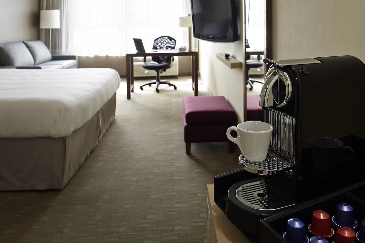 A hotel room with a bed, a desk, a chair, a television, and a coffee machine.