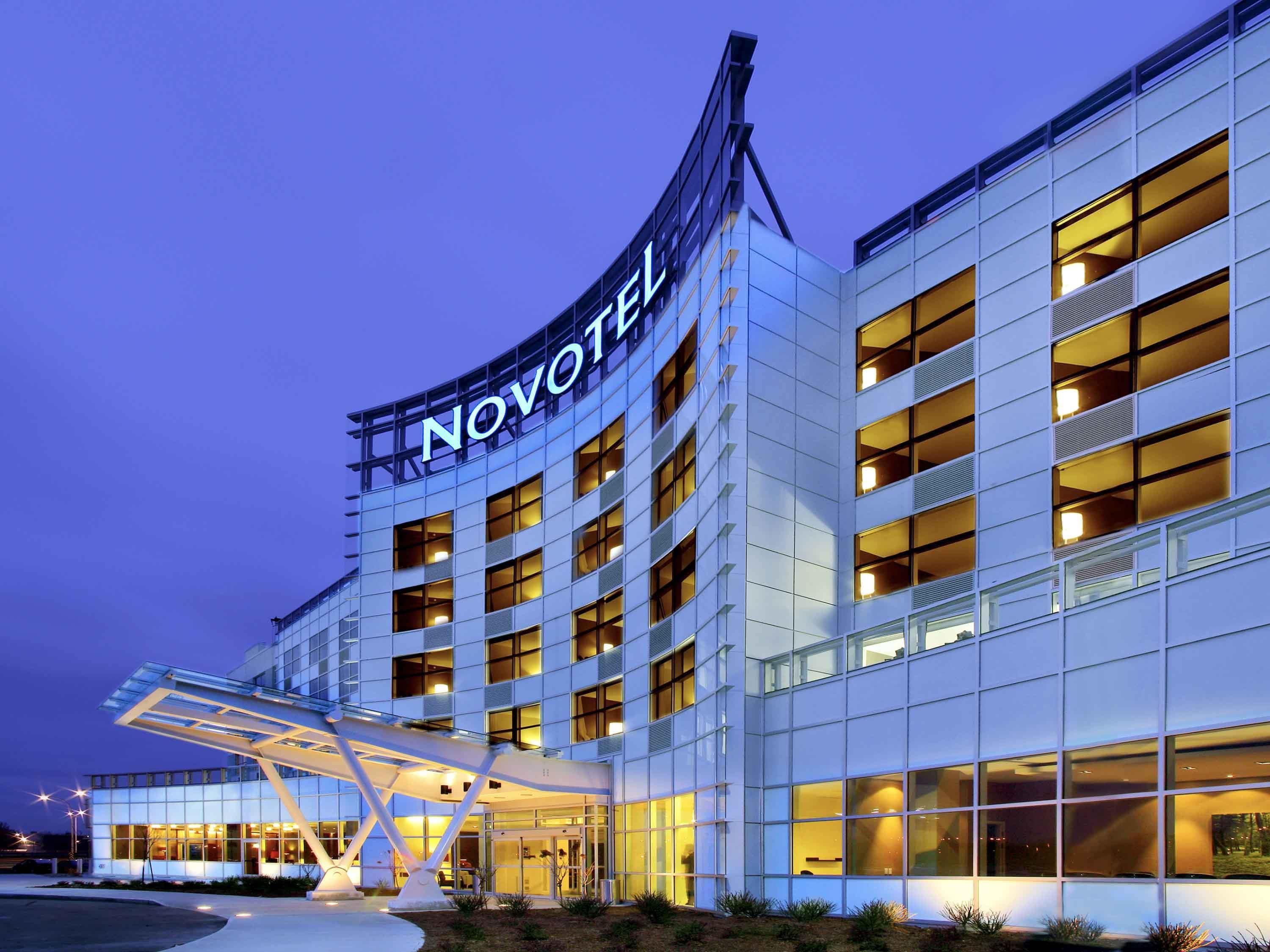Un moderno edificio de hotel con un llamativo letrero de 'NOVOTEL', varios pisos y una zona de acceso cubierta.