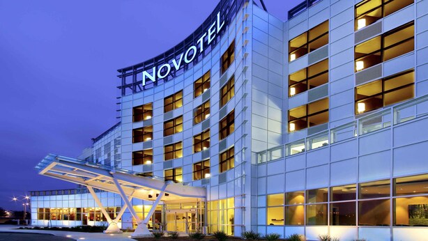 A modern hotel building with a prominent 'NOVOTEL' sign, multiple floors, and a covered entrance area. - Novotel Montreal Aeroport (Montreal)
