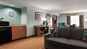 A hotel room with a kitchenette, a sofa with patterned cushions, a desk with a chair, and a dining area with a table and chairs.