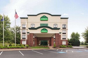 Un hotel Wingate by Wyndham con fachada de ladrillo, detalles en verde y un estacionamiento al frente.