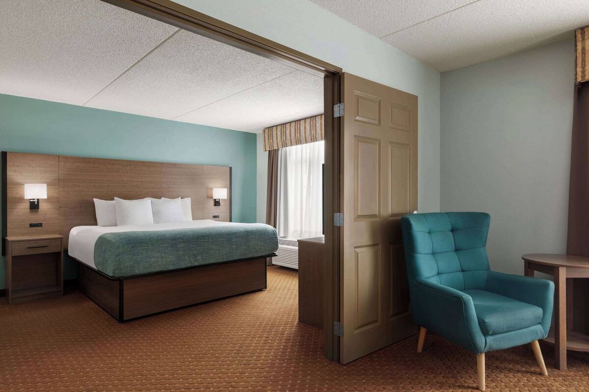 Une chambre d’hôtel avec un lit, une chaise, une table de chevet et une fenêtre avec des rideaux.