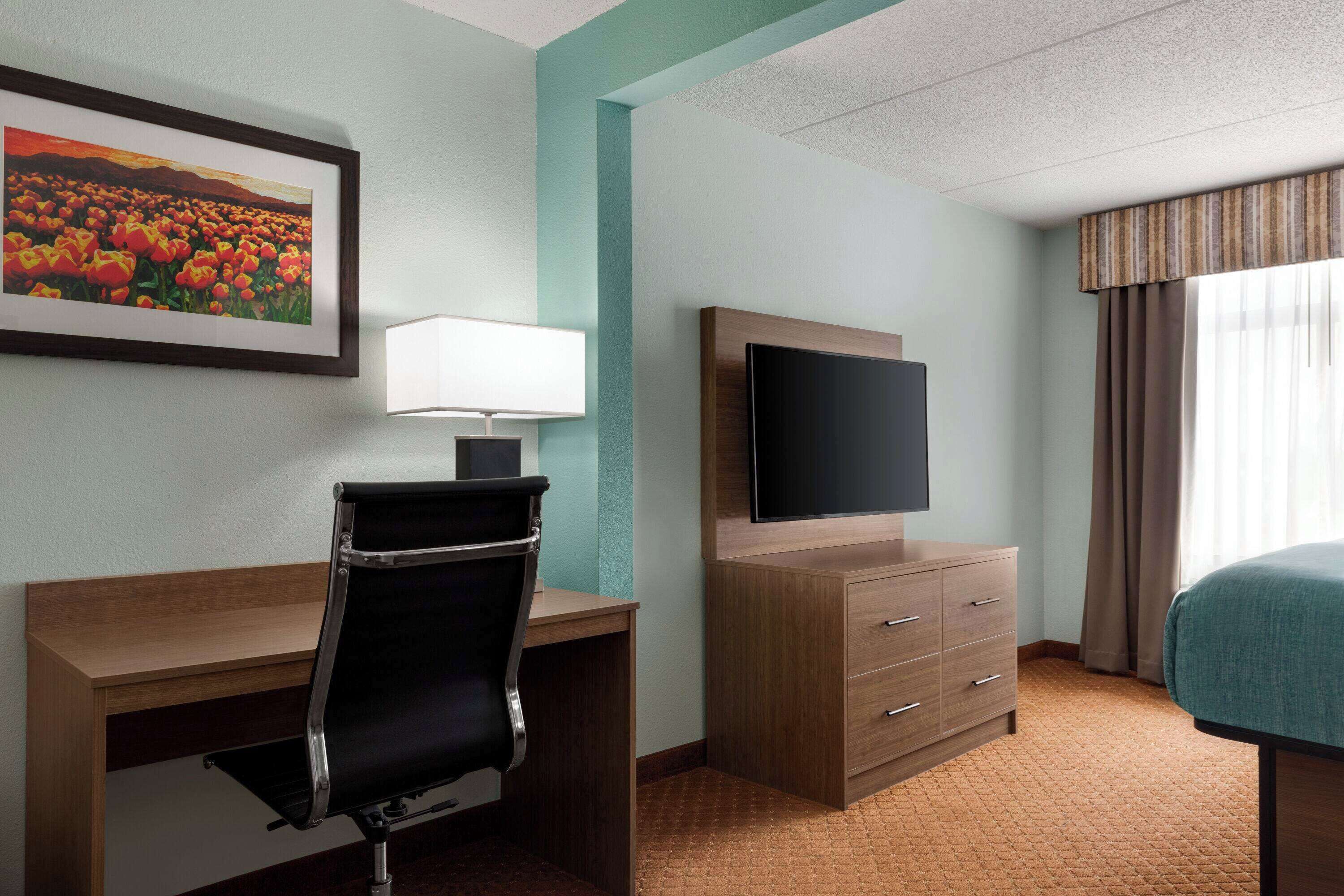 A hotel room with a desk, chair, television, and a bed.