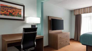 A hotel room with a desk, chair, television, and a bed.