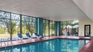An indoor swimming pool with clear views of the outdoors, surrounded by large windows and equipped with lounge chairs.