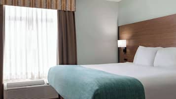 Una habitación de hotel con una cama grande, una ventana con cortinas, una lámpara de pared y un cabecero de madera.