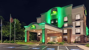 A Wingate by Wyndham hotel with a green-lit entrance, handicap parking, and a flag in the foreground.