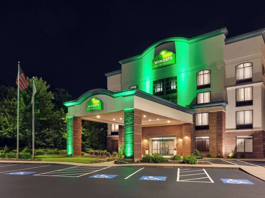 A Wingate by Wyndham hotel with a green-lit entrance, handicap parking, and a flag in the foreground.