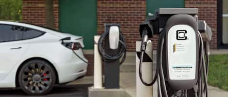 En hvid elbil-ladestation med et kabel tilsluttet en Tesla Model 3, der holder i nærheden.